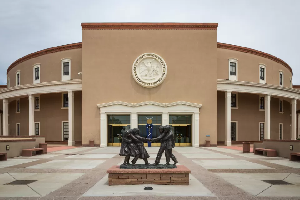 The New Mexico State Capitol building, with a statue of small children playing in the foreground.
